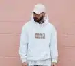 man wearing white pullover hoodie standing against the wall
