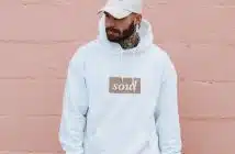 man wearing white pullover hoodie standing against the wall