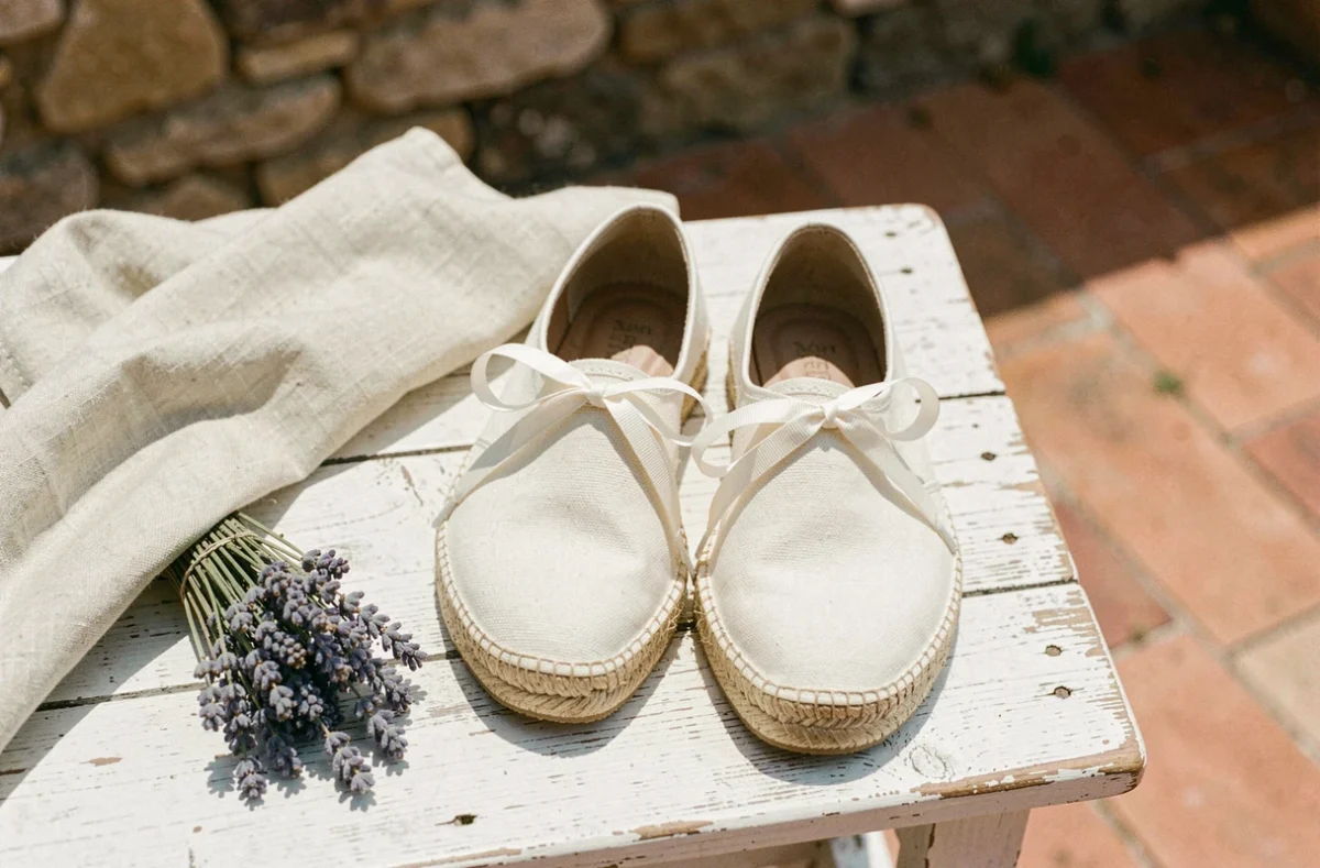 Espadrilles de créateur en toile crème avec semelle en jute posées sur une terrasse provençale en bois patiné, style vue de dessus